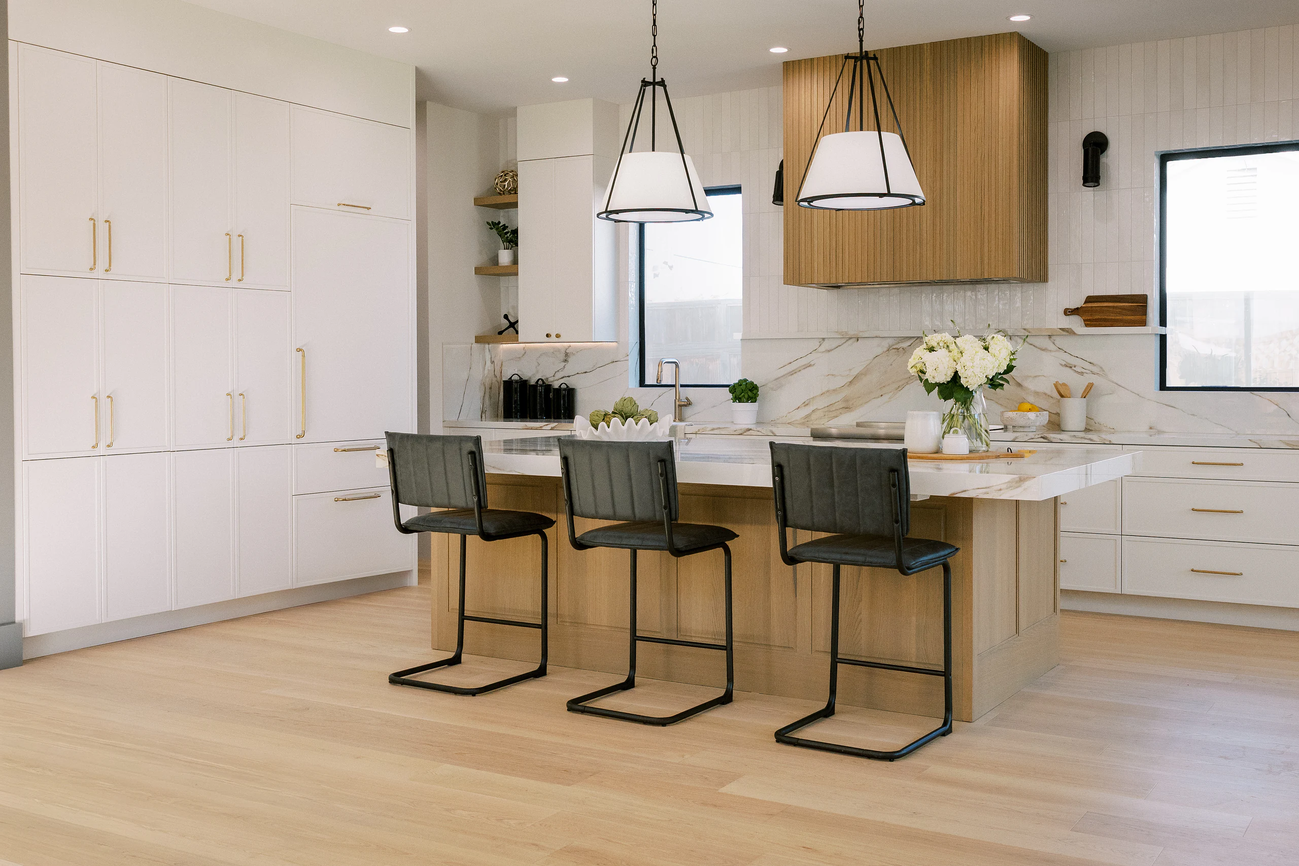 Bright modern kitchen with a fluted white oak hood and black counter stools
