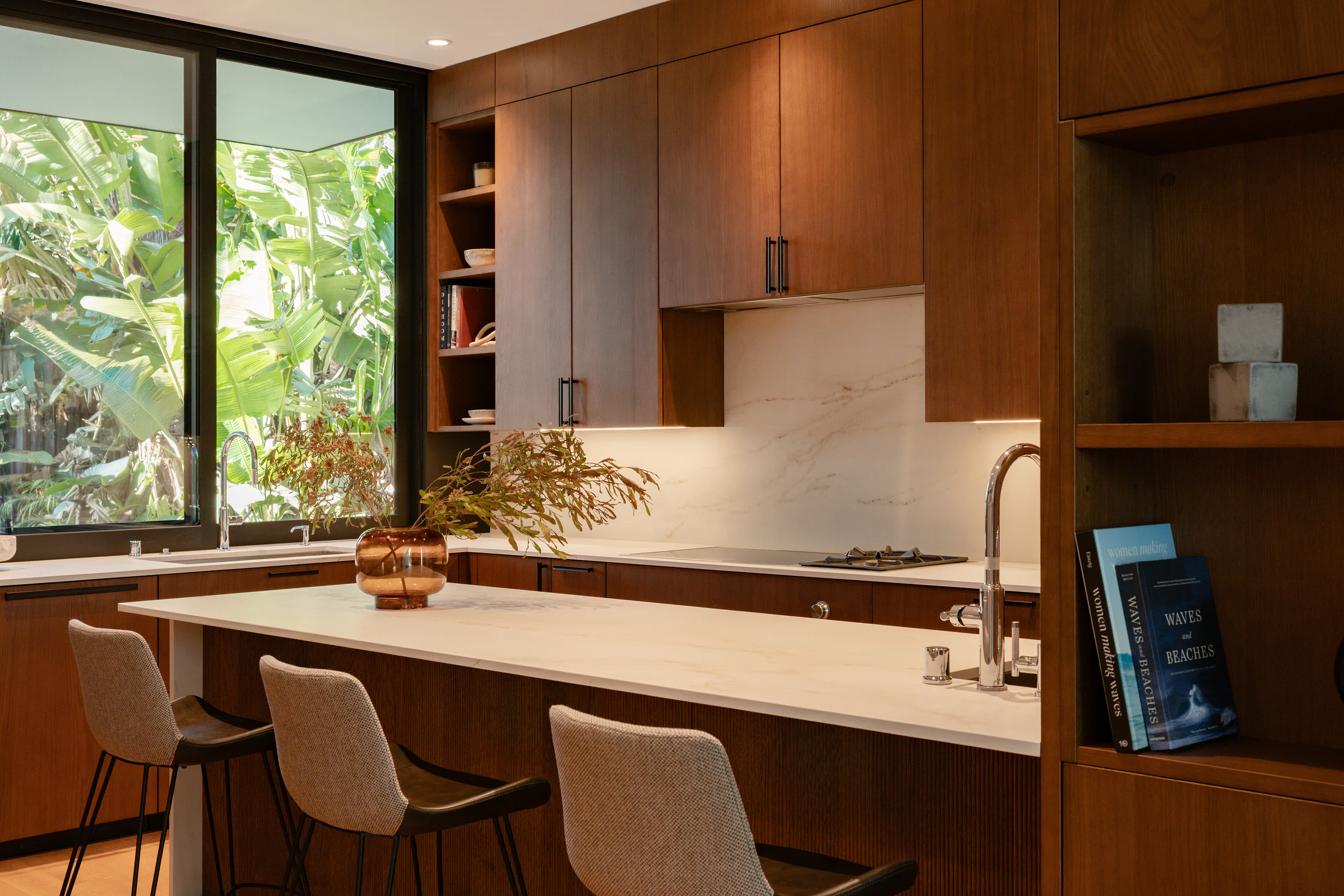 Warm DOCA walnut kitchen with a long island, full-height glazing, and clean horizontal lines