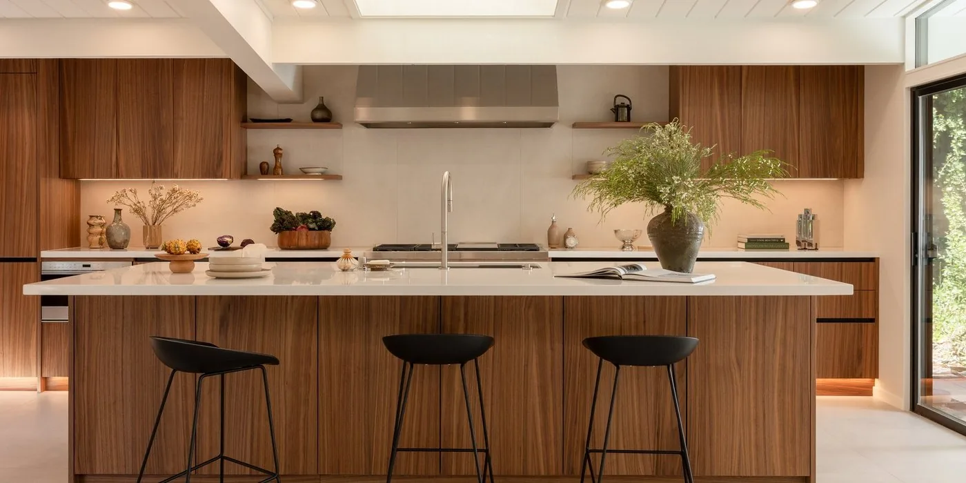 Open Eichler kitchen with walnut island, stainless hood and a glass wall to the garden