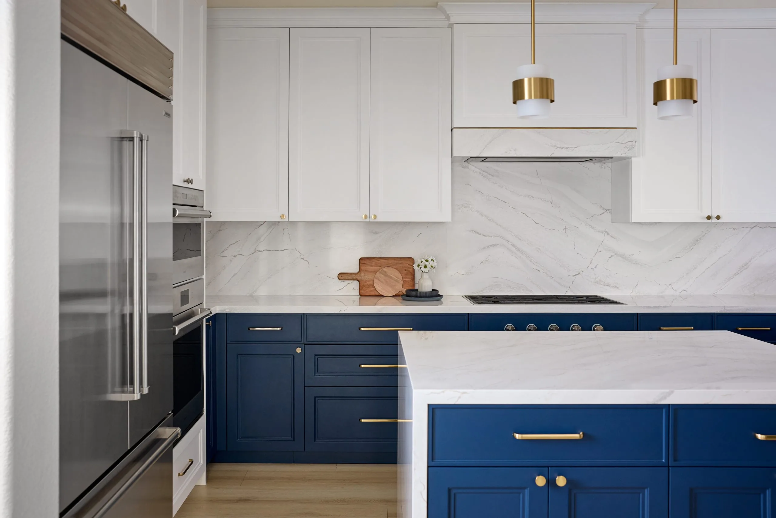 Navy and white kitchen with a marble waterfall island and brass pendants