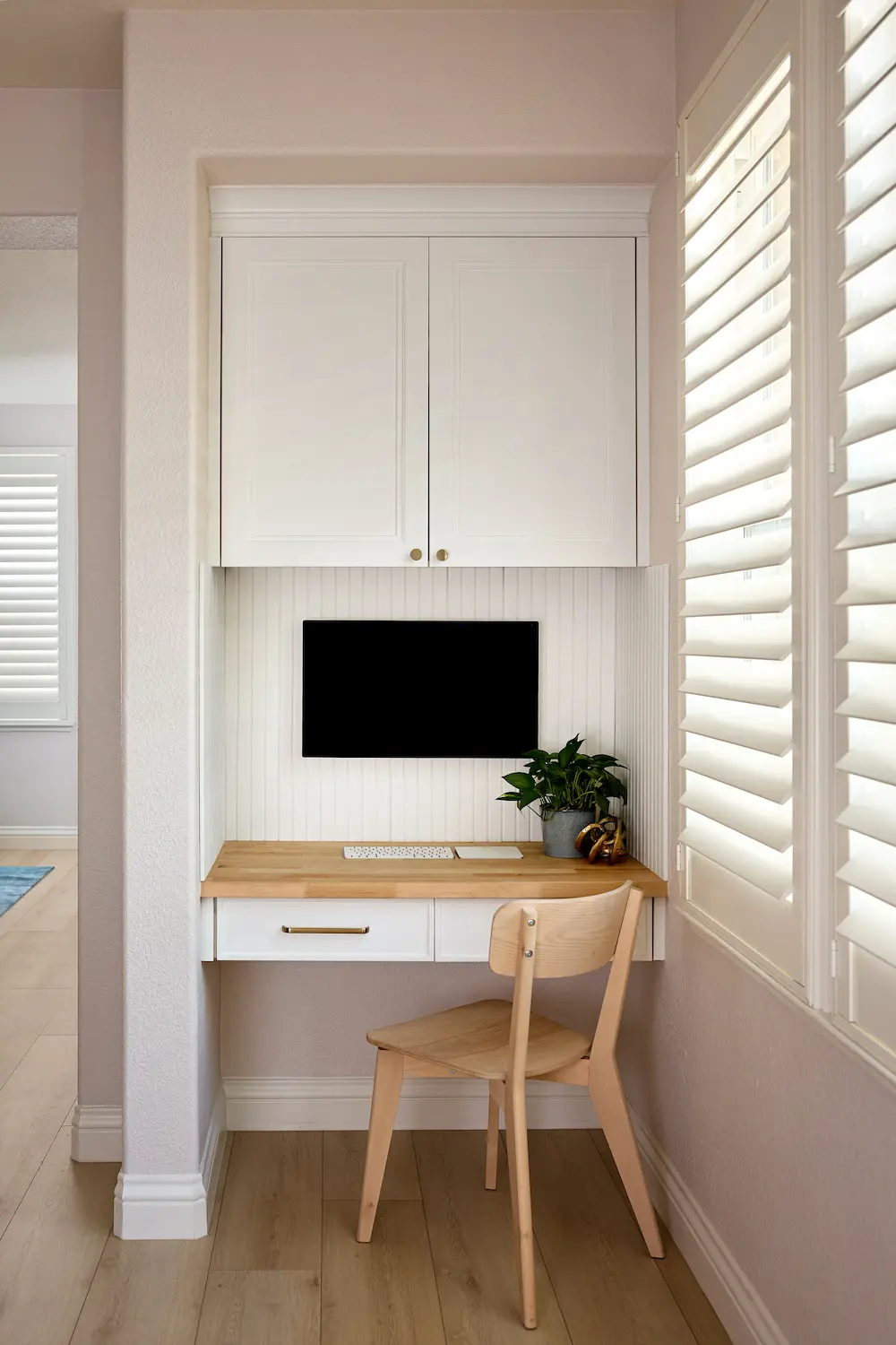 Built-in wood desk nook with white cabinetry, wall-mounted TV, and window shutters