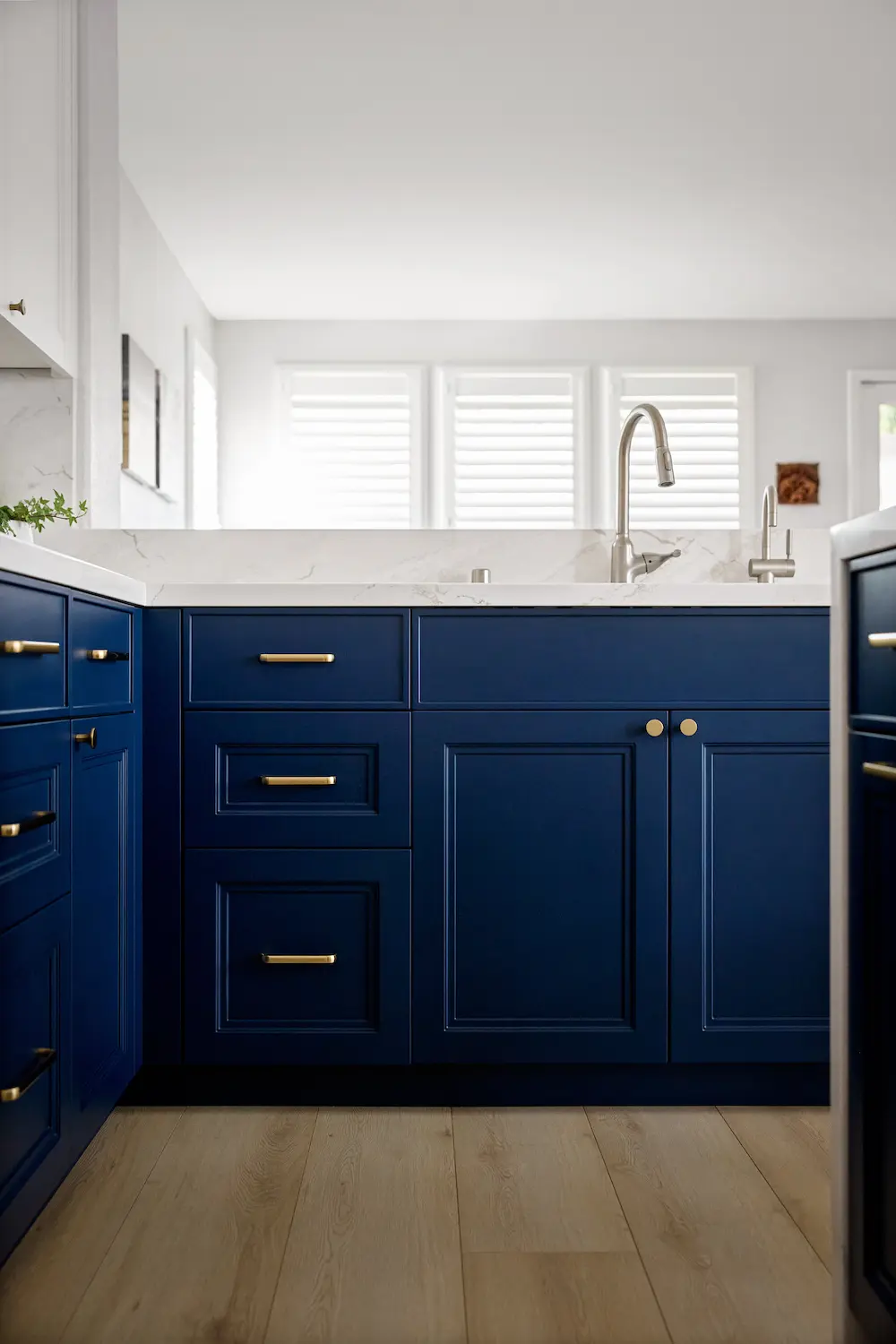 Close-up of navy sink base cabinet with brass hardware and window shutters behind