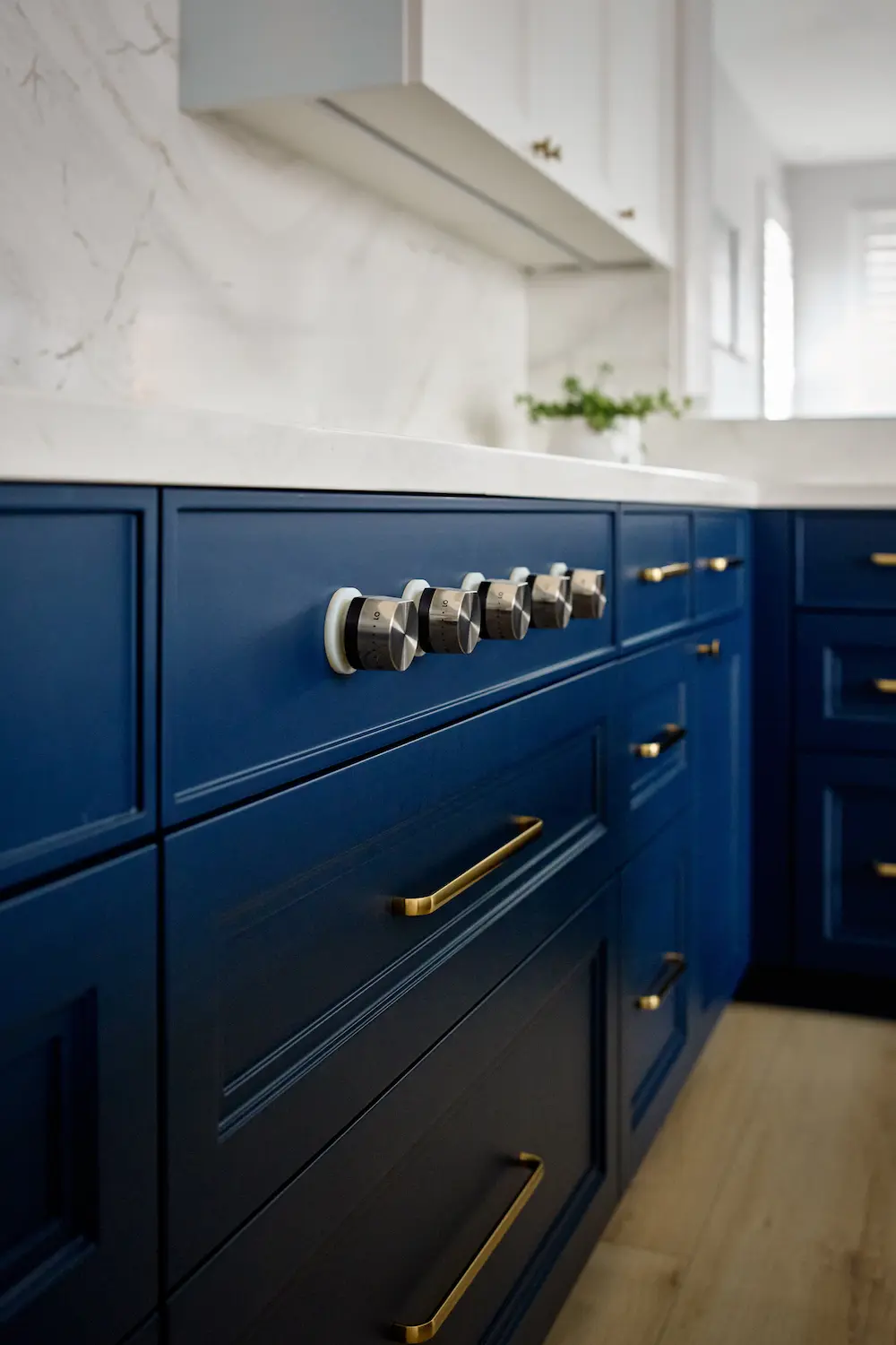 Detail shot of navy range cabinetry with brass drawer pulls and stainless cooktop knobs