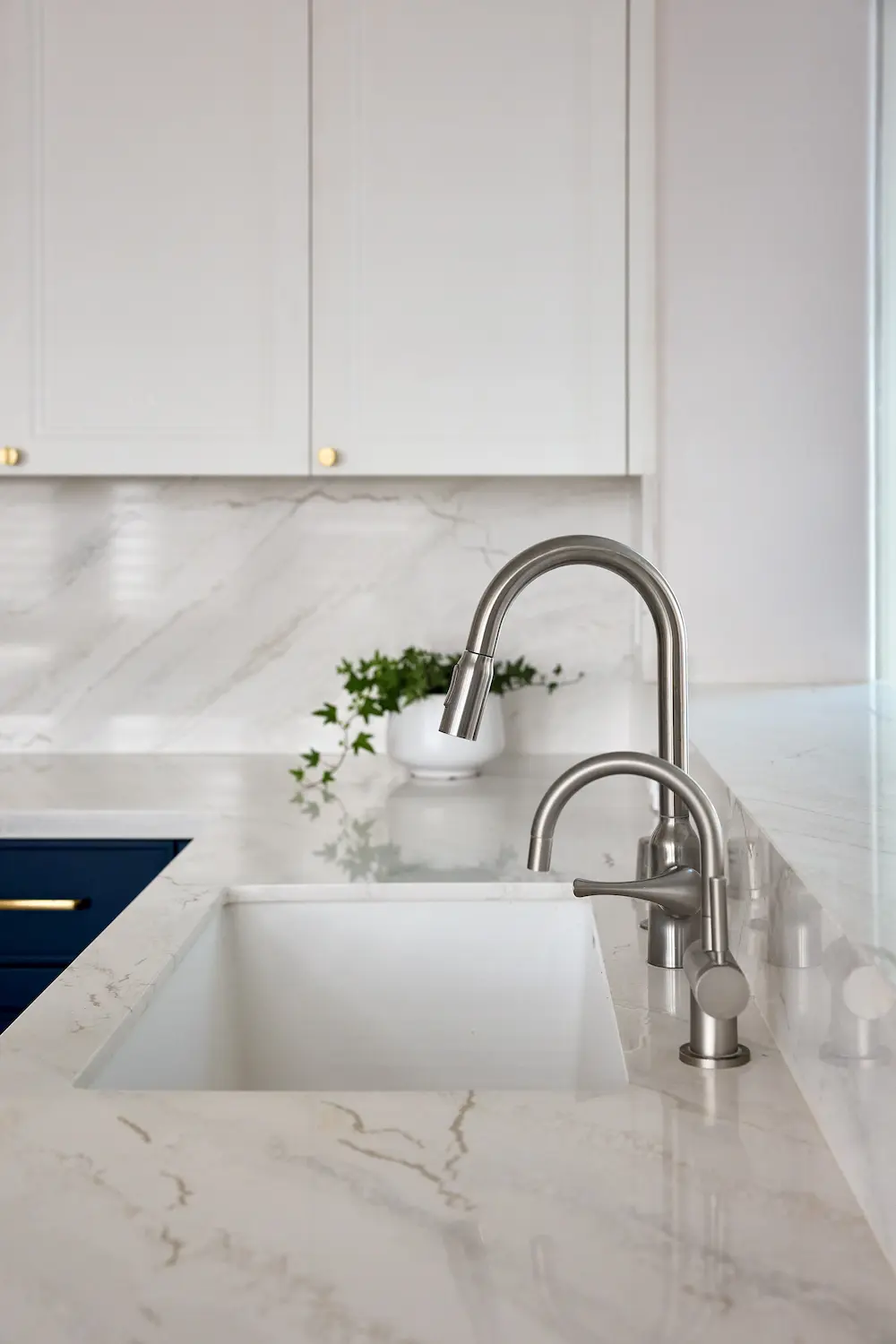 Close-up of stainless kitchen faucet and sink on white marble countertop