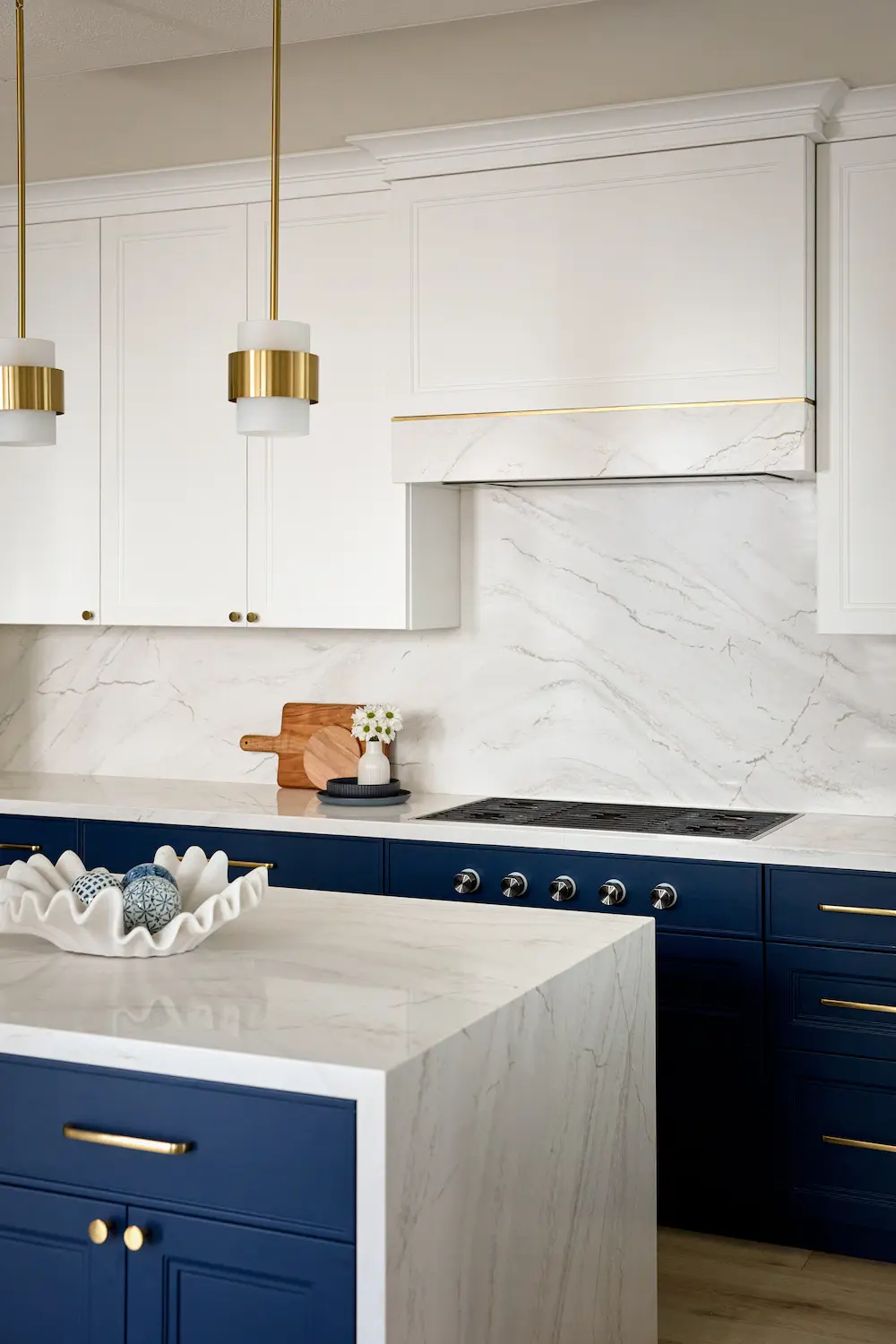 Marble backsplash and range hood detail with brass pendant lights and navy cabinetry