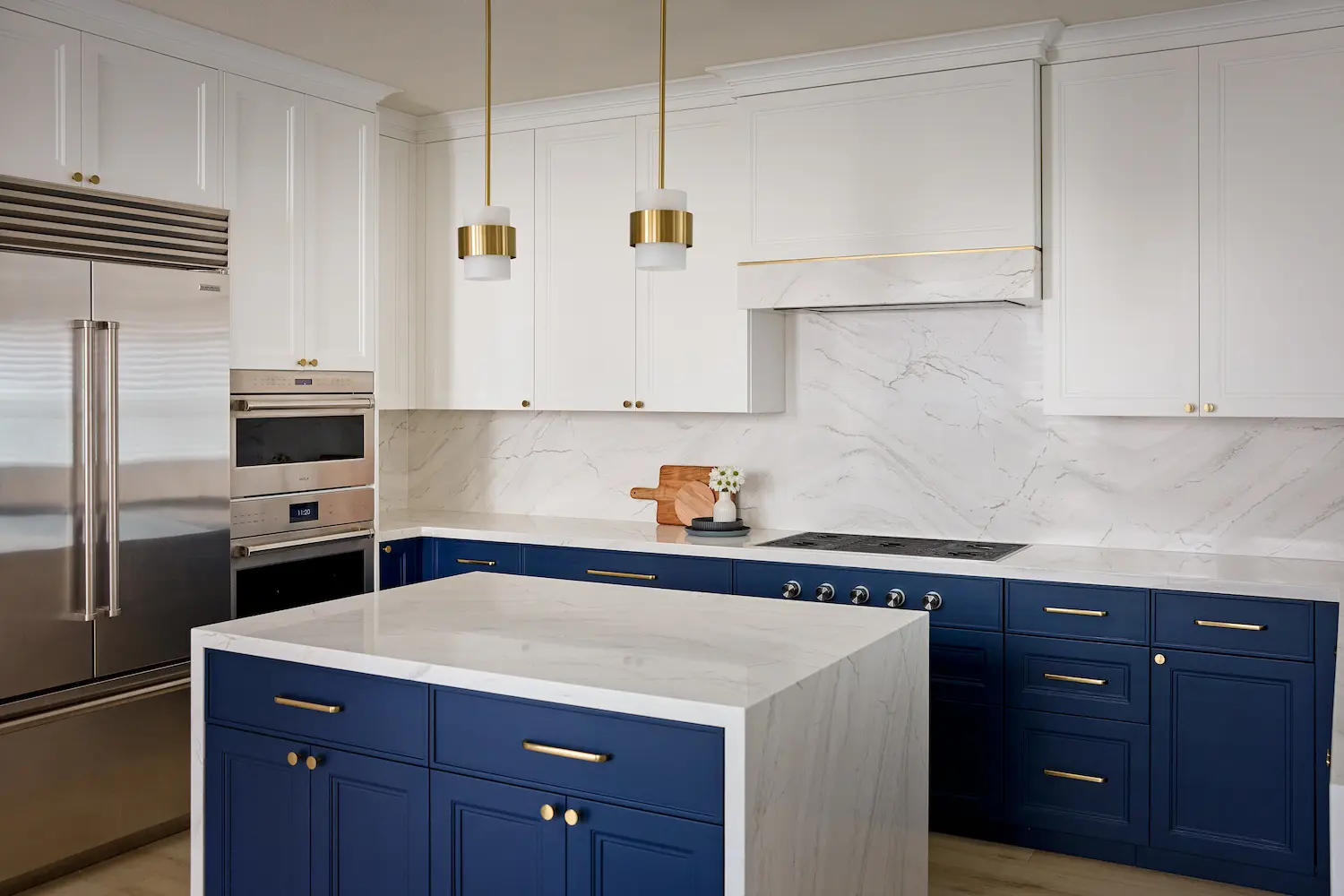 Wide kitchen view with navy island, marble waterfall countertop, stainless refrigerator, and brass pendants