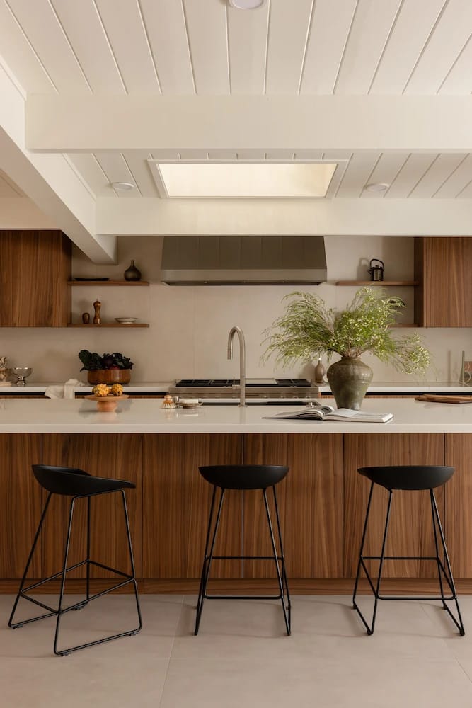 Kitchen island with three black stools facing the range wall under a skylight
