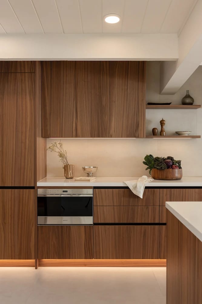 Stainless range and hood framed by wood drawers and floating shelves under a skylight