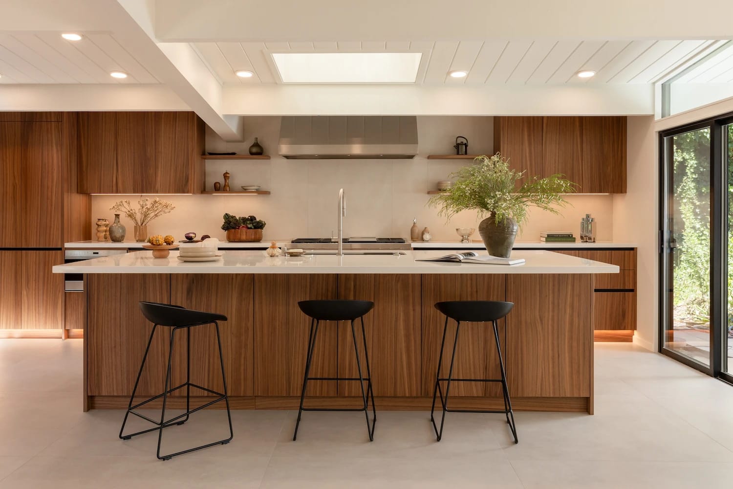 Eichler kitchen with warm wood DOCA cabinets, a long white island and black stools