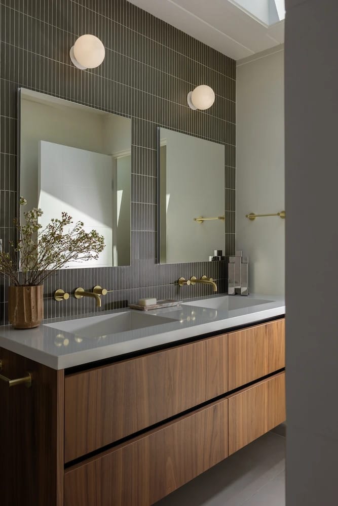 Floating wood double vanity below two mirrors on a green stacked-tile wall