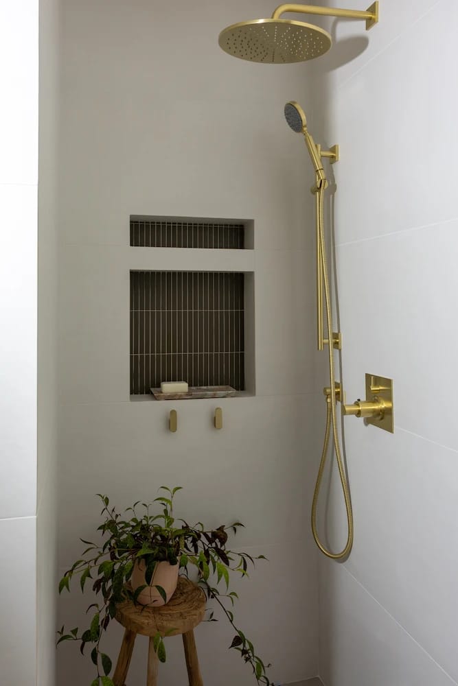 Walk-in shower with a brass rain head, handheld wand and tiled niche