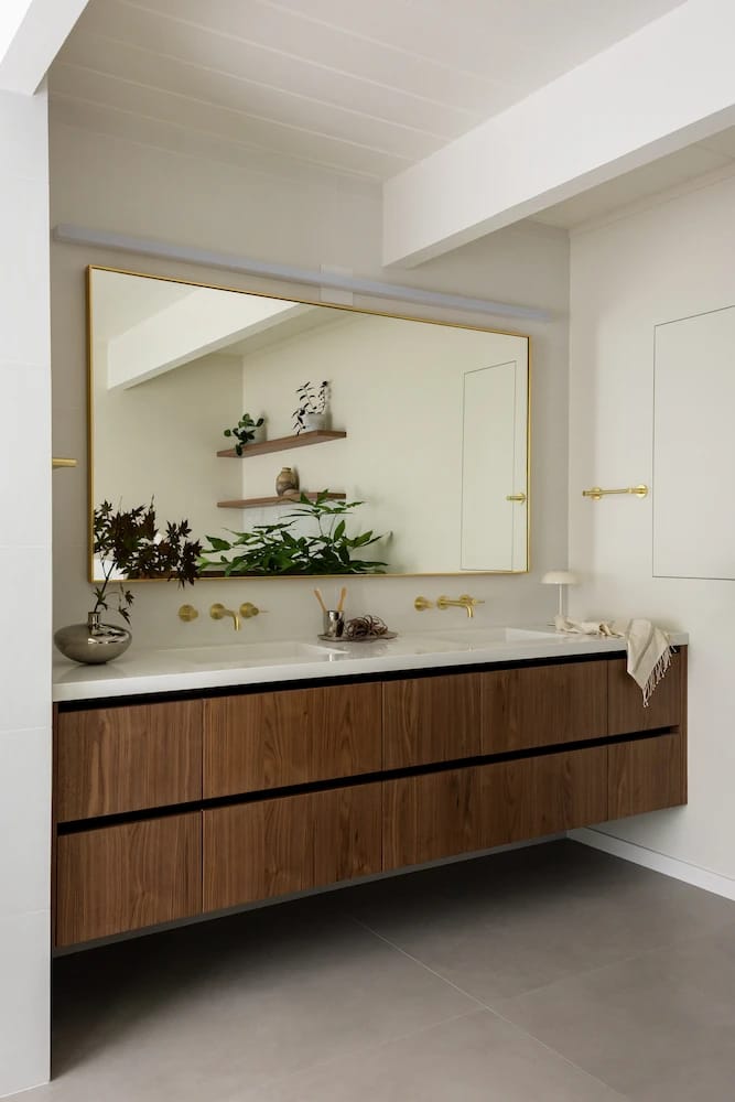 Floating wood double vanity with a brass-framed mirror and wall-mounted brass faucets