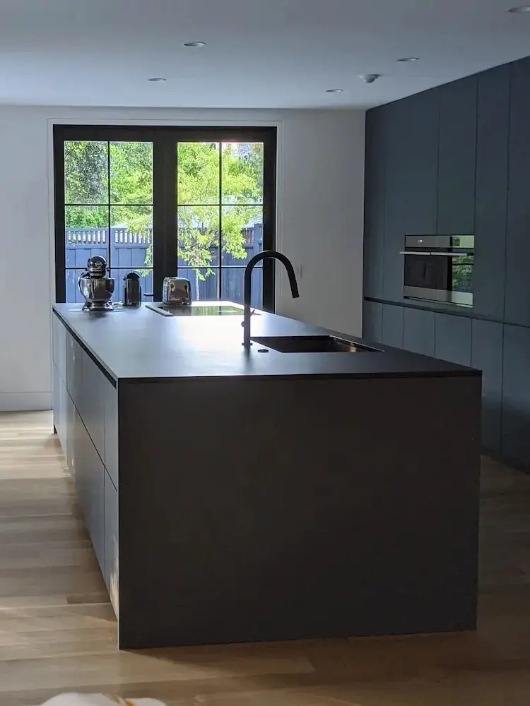 Modern open kitchen with black countertops, midnight blue cabinetry, overlooking the backyard