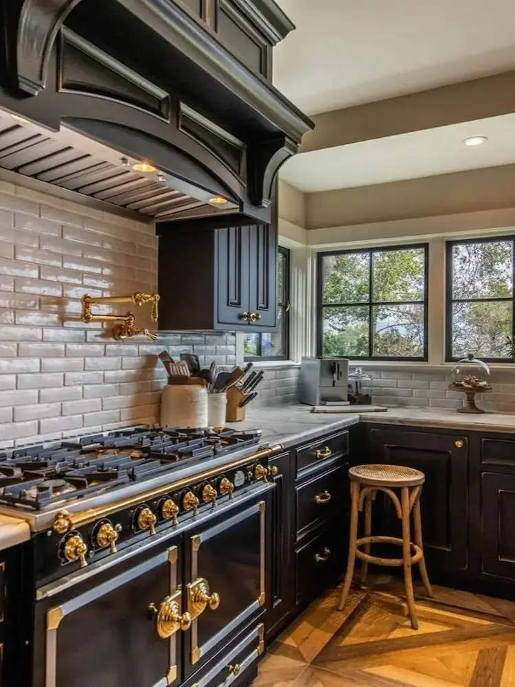 Traditional kitchen with black cabinetry, gold hardware, and large gas range with marble countertops