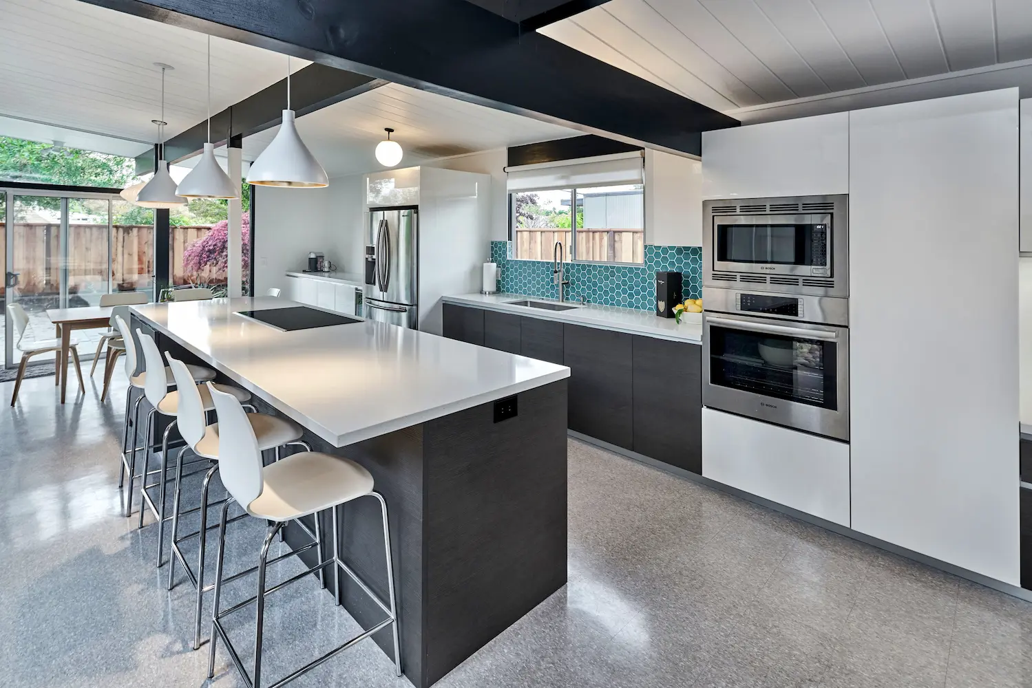 Spacious mid-century modern kitchen with an island seating area, minimalist white cabinetry, and integrated stainless steel appliances