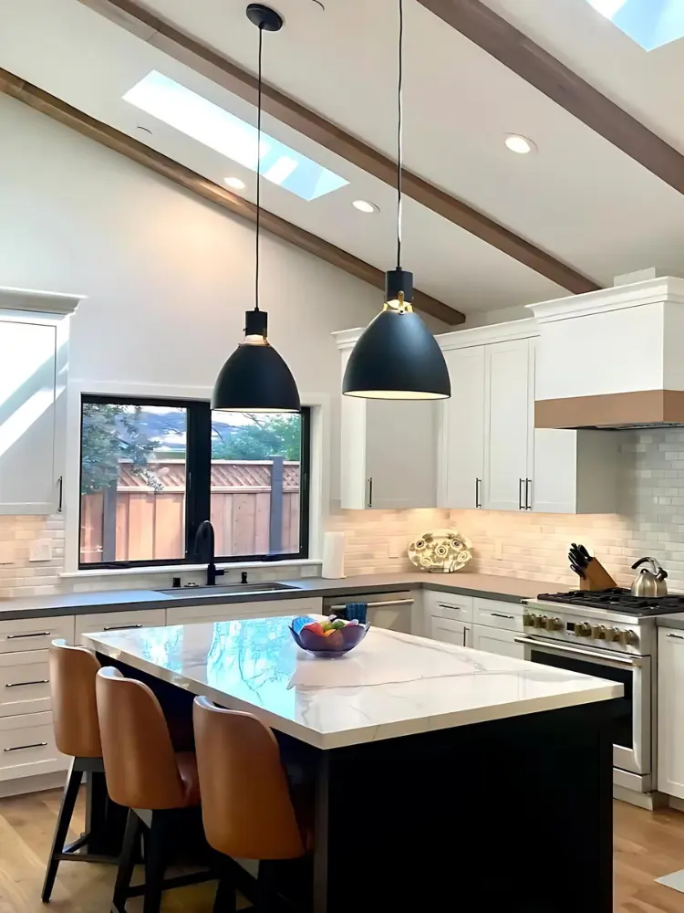 Kitchen with vaulted ceilings, large island, black fixtures, and natural light streaming through skylights