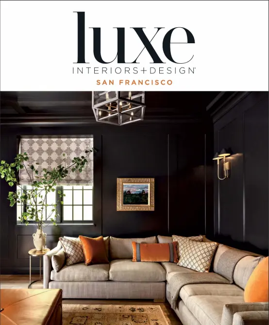 Cover of Luxe Interiors + Design magazine, San Francisco edition, featuring a luxurious living room with dark walls, a light gray sectional sofa adorned with orange and patterned pillows, a geometric pendant light, and a vibrant indoor plant near a window with patterned shades