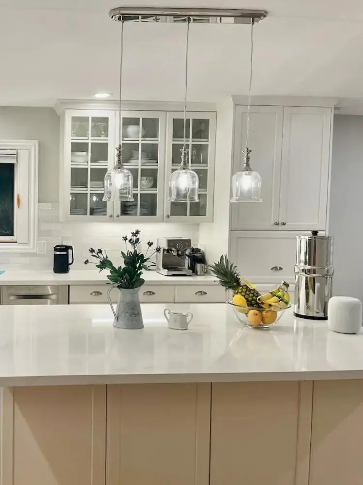 Elegant transitional kitchen space showcasing bright white finishes, sleek appliances, and a central island with decorative pendant lights
