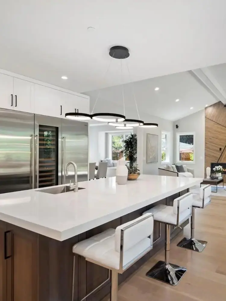 Open-concept kitchen and living area with white cabinetry, large island, sleek countertops, and modern pendant lighting