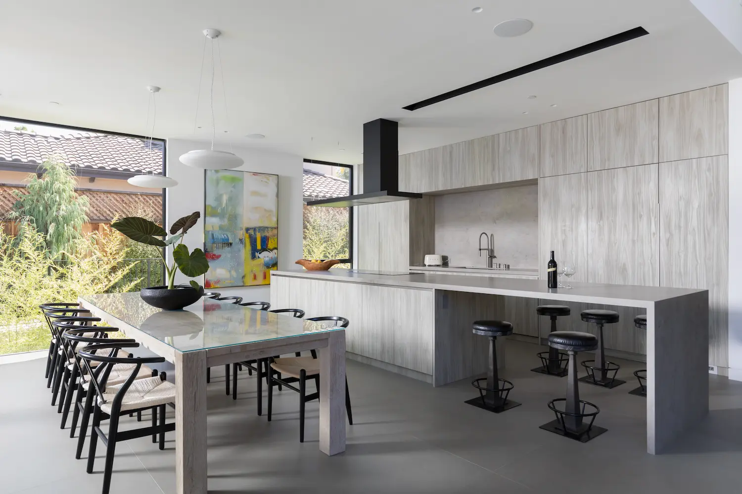 Modern open-concept kitchen with sleek cabinetry, integrated appliances, and a spacious island complemented by a glass dining table and vibrant artwork