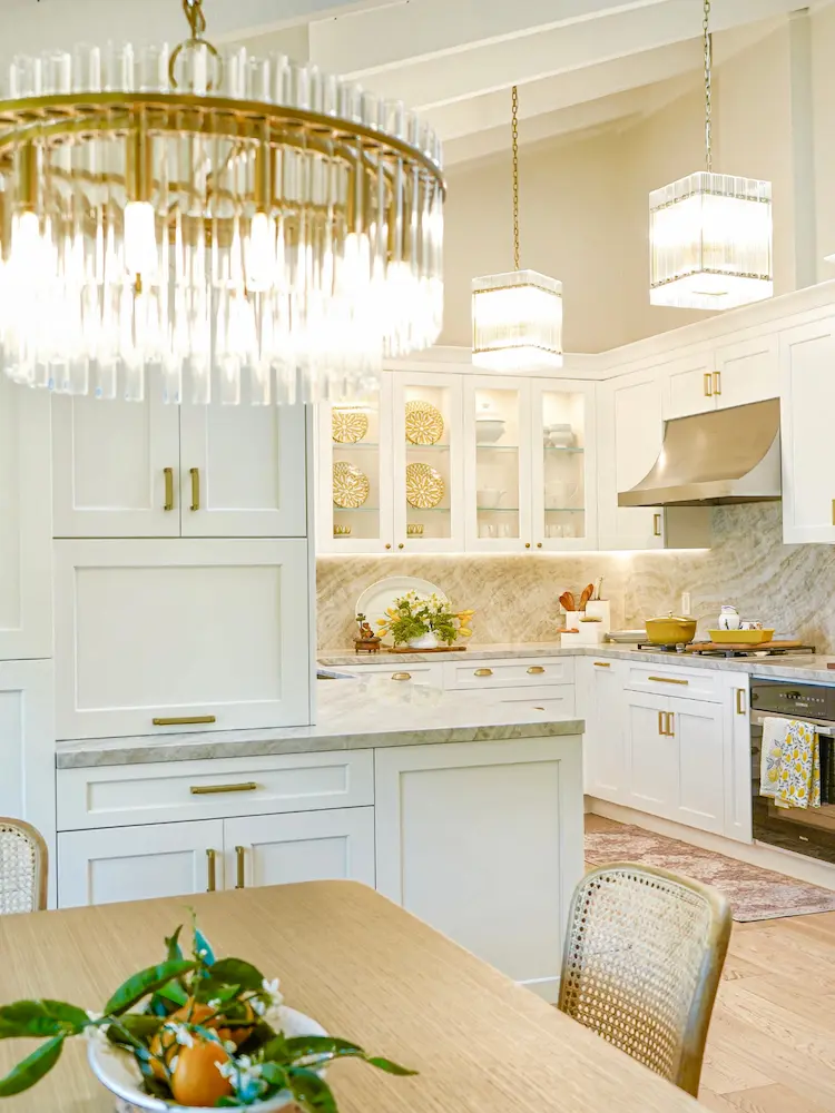 Spacious transitional kitchen featuring white cabinets, gold hardware, and a large statement chandelier over a wood dining table