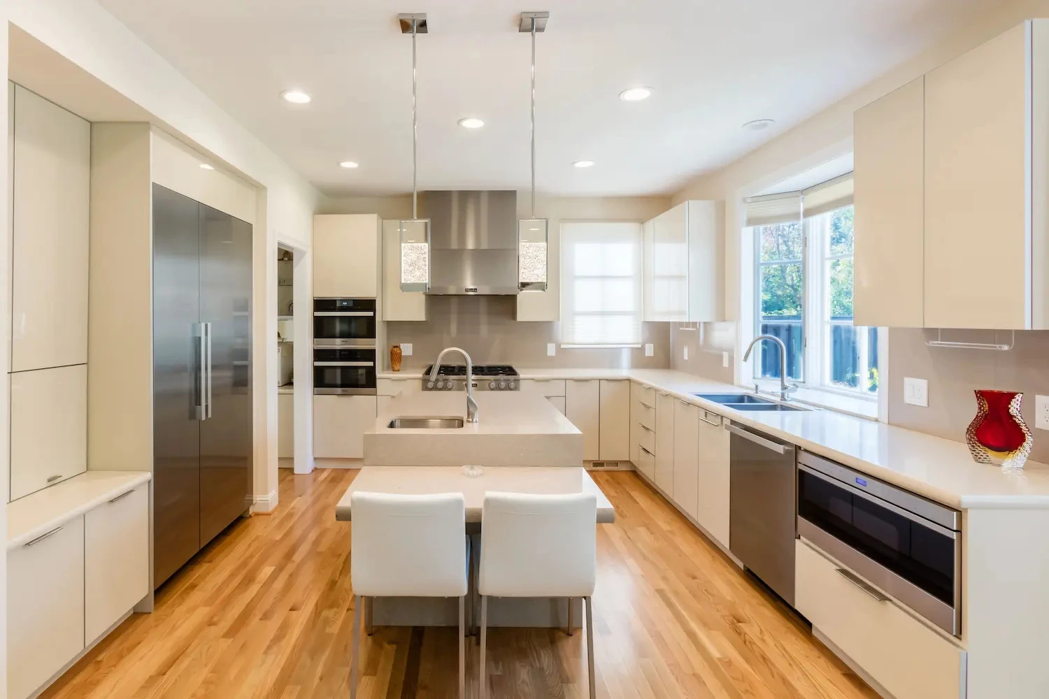 Sleek contemporary kitchen with integrated appliances, double wall ovens, light wood flooring, and a central island with attached seating