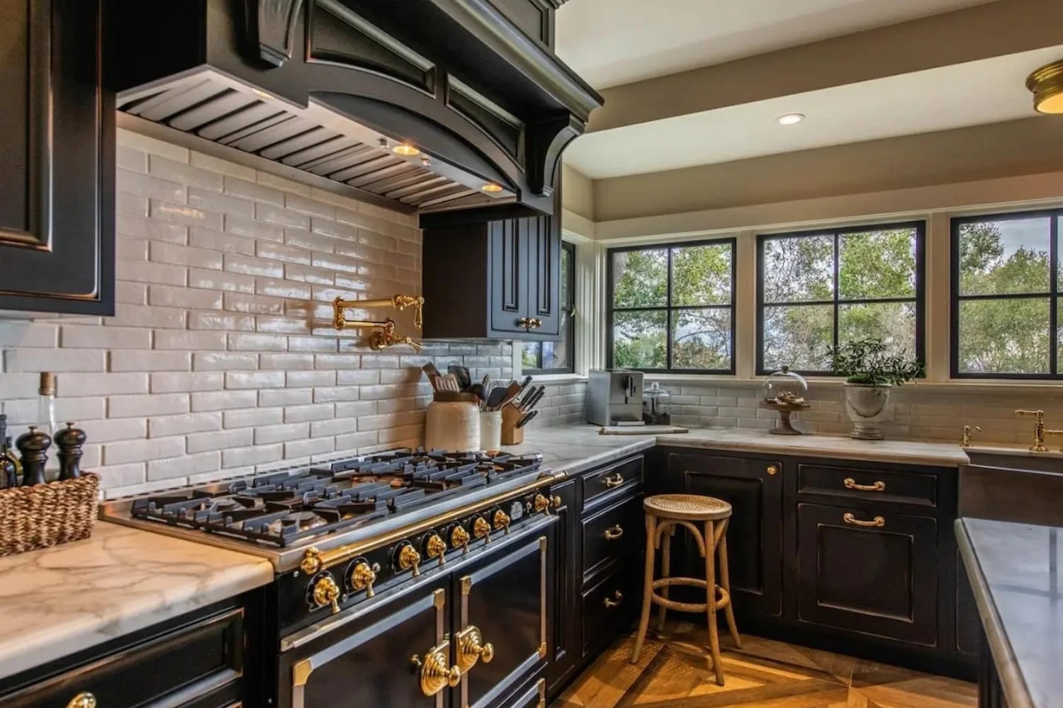 Black and gold kitchen featuring luxury range, white marble countertops, and subway tile backsplash under natural light