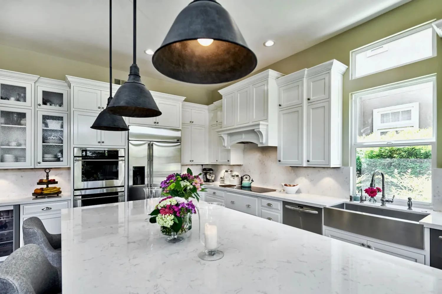 Traditional white kitchen with farmhouse sink, marble counters, and oversized pendant lighting over the island
