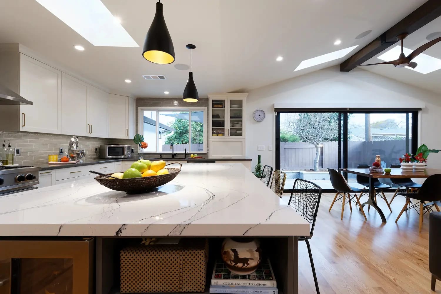 Bright modern kitchen with skylights, large island with veined quartz countertops, and wide-plank wood flooring
