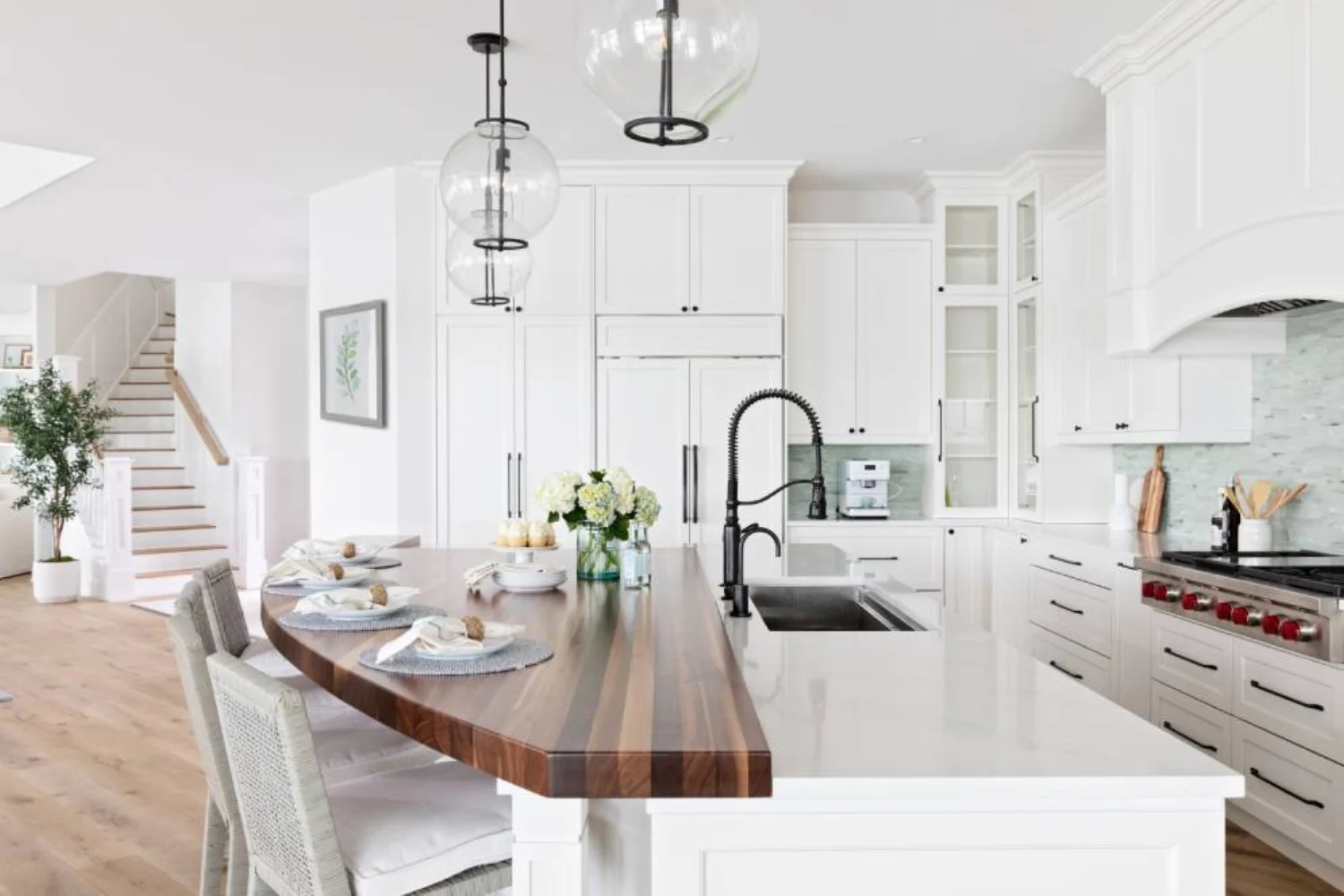 Bright white kitchen with a curved walnut island extension, glass pendant lights, and built-in appliances for a coastal feel