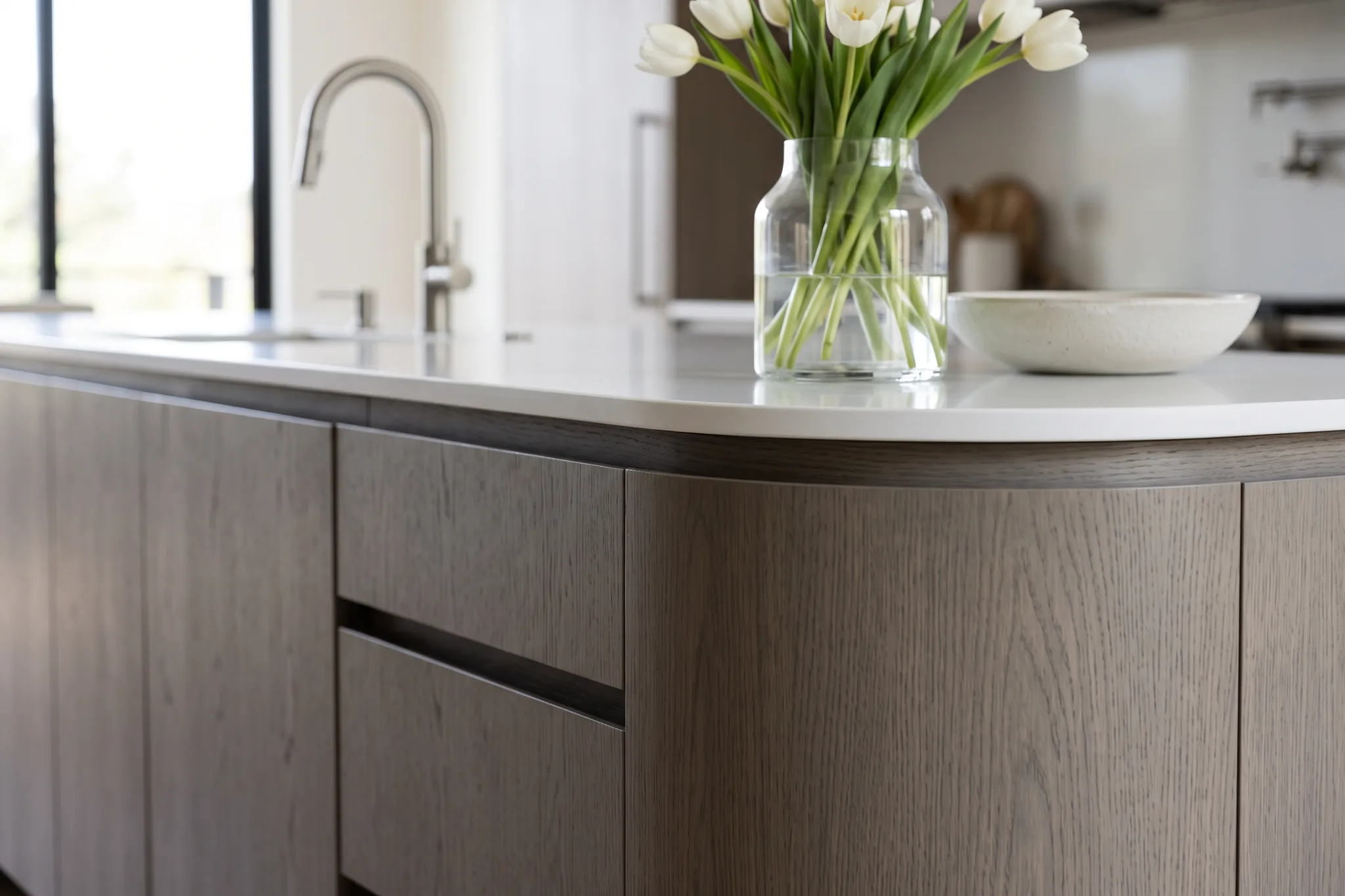 Curved island with handleless gray oak drawers and a thin white top