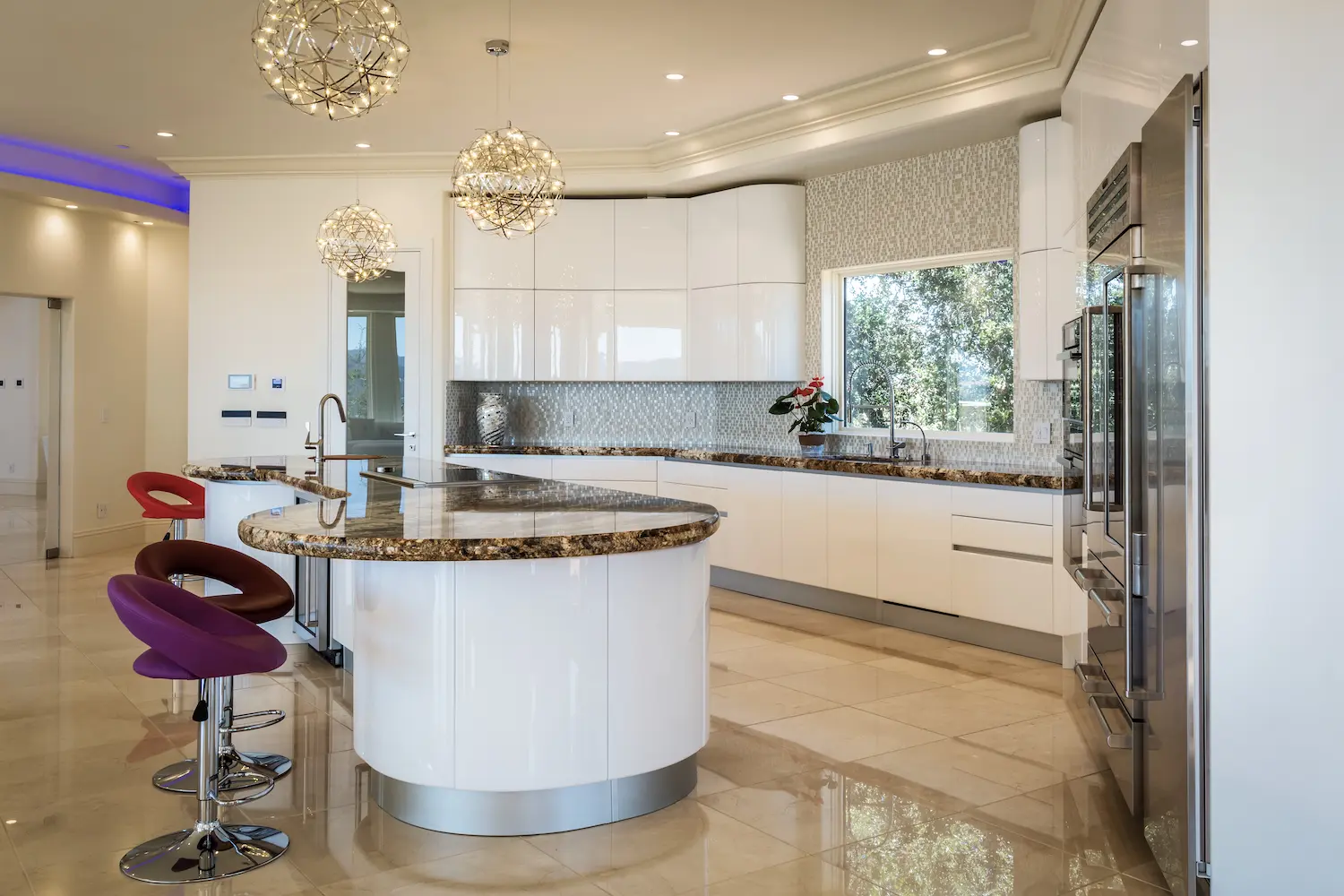 Kitchen featuring glossy white cabinets, curved countertops, and unique pendant lights, providing an elegant cooking space