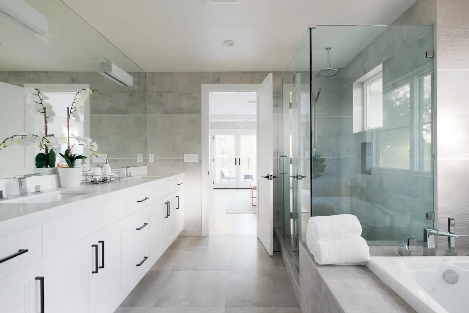 Contemporary bathroom with double sink vanity, glass-enclosed shower, and neutral tones, featuring white cabinetry and modern fixtures