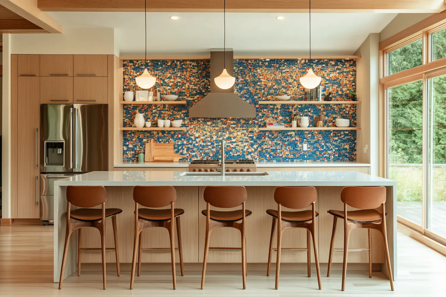 Mid-century modern kitchen with a vibrant mosaic backsplash, sleek wooden cabinetry, and a spacious island with modern bar stools, bathed in natural light from large windows