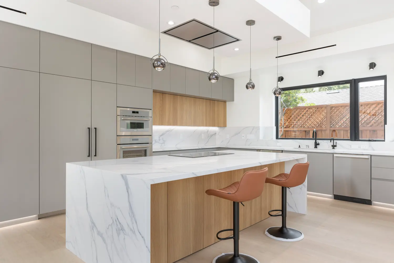 Kitchen design featuring a white marble waterfall island, light wood cabinetry, and gray flat-panel cabinets with integrated appliances